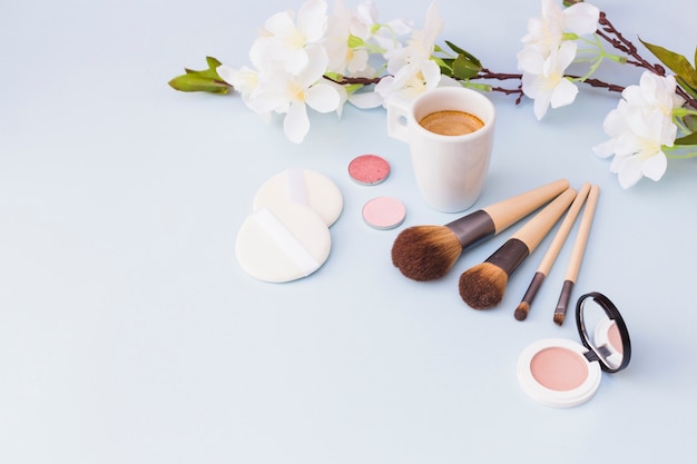 Taza de café con producto de cosméticos y ramita de flor blanca sobre fondo blanco