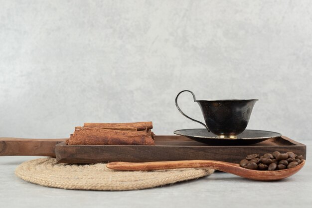 Taza de café con ramas de canela en tablero oscuro y granos de café