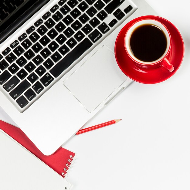 Taza de café roja en una computadora portátil abierta sobre fondo blanco