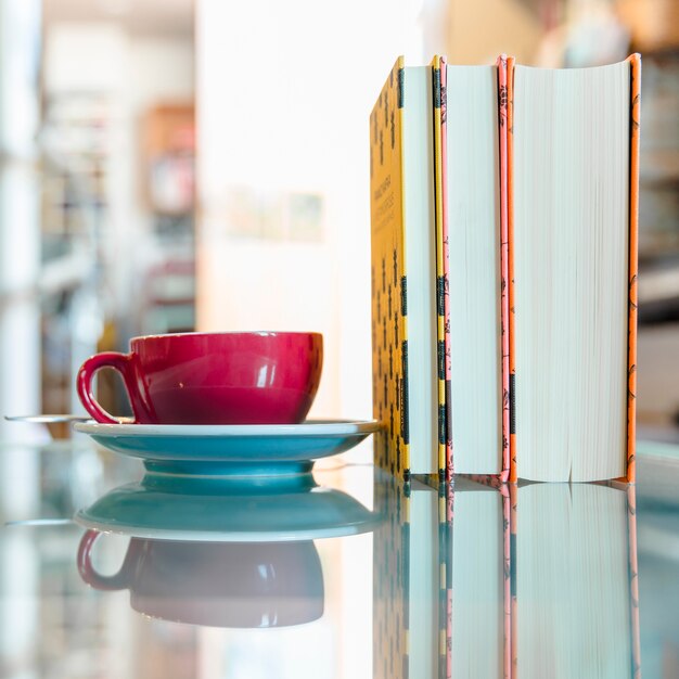 Taza de café rojo y libro sobre vidrio reflectante