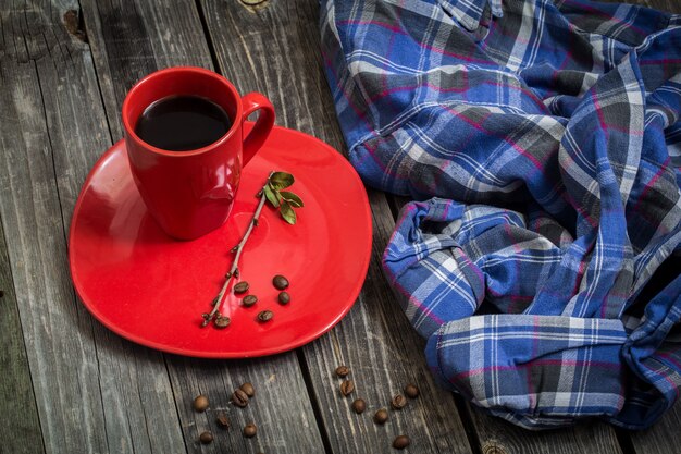 Taza de café rojo en un plato sobre un hermoso fondo de madera, bebidas, granos de café esparcidos