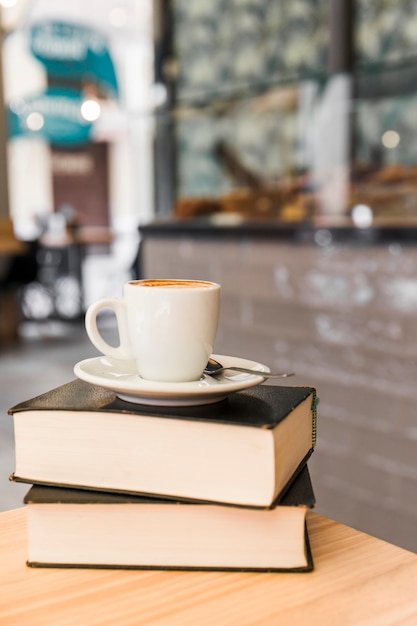 Taza de café sobre libros en la mesa de madera
