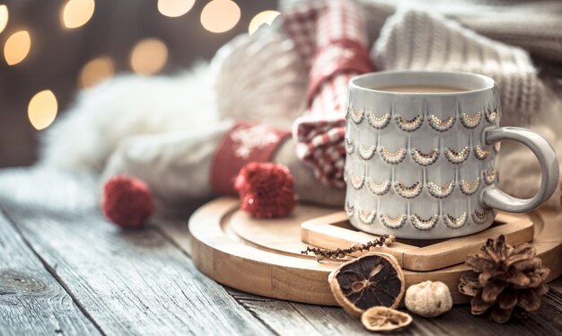 Taza de café sobre luces de Navidad bokeh en casa en mesa de madera con suéter en una pared y decoraciones. Decoración navideña