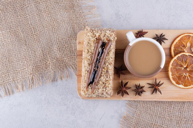 Taza de café, tarta y rodajas de naranja sobre tabla de madera.