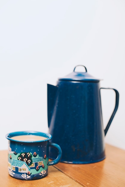 Taza de café y tetera borrosa en mesa de madera con fondo blanco