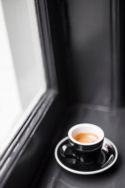 Taza de café vacía negra con manchas de café en el alféizar de la ventana