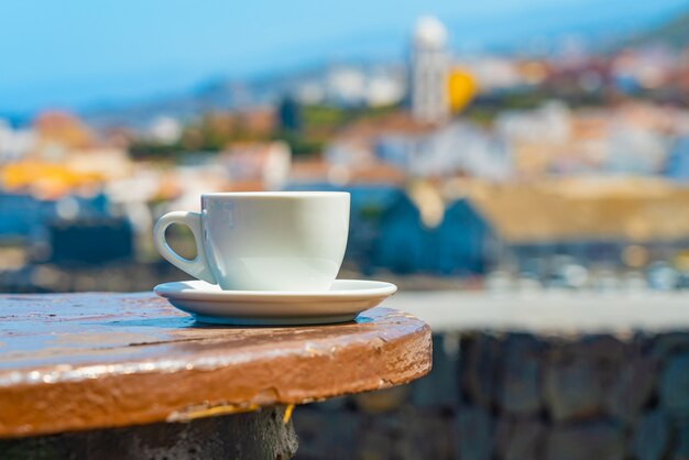 Taza de café con una vista borrosa de un pueblo de Garachico en la orilla del océano