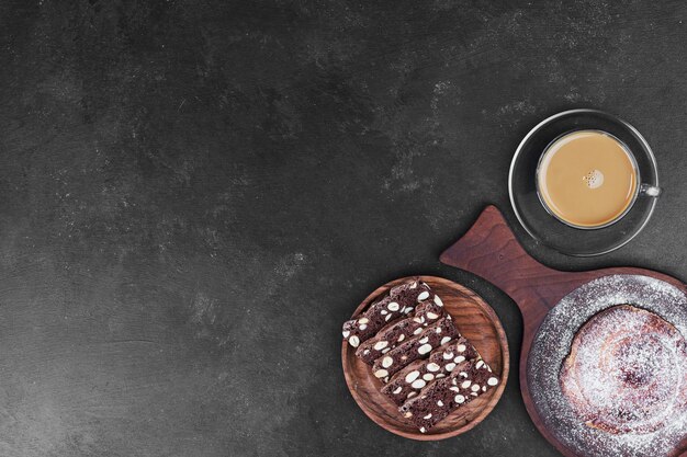 Una taza de capuchino con galleta de cacao y bollo dulce.