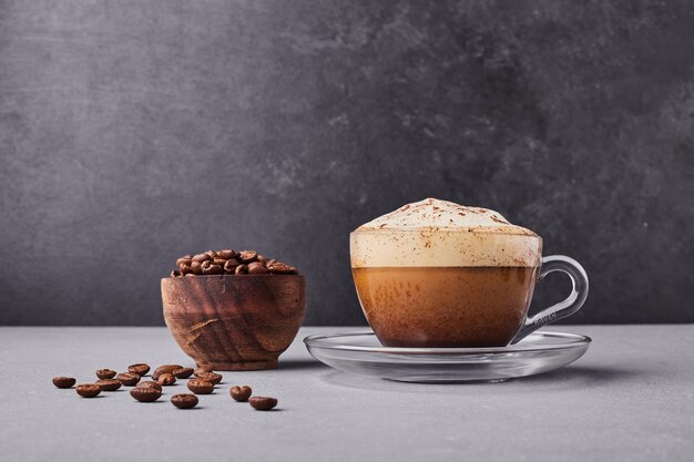 Una taza de capuchino con granos de café alrededor.