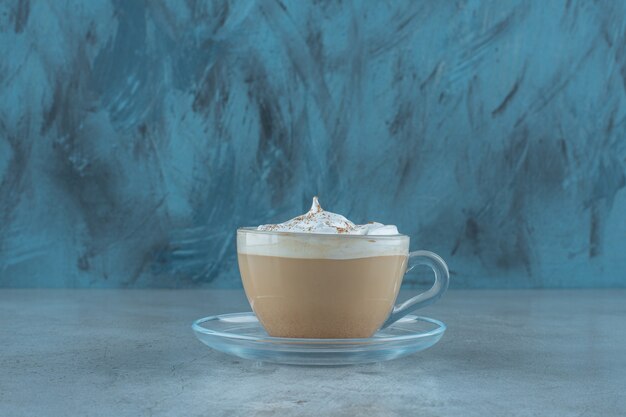 Una taza de capuchino en un platillo, sobre la mesa azul.