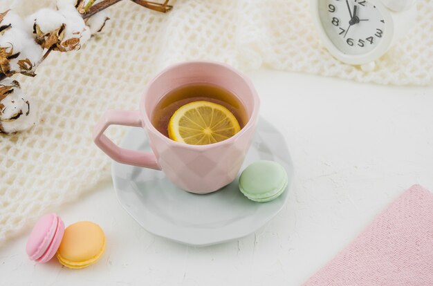 Taza de cerámica rosa con té de limón y macarrones sobre fondo blanco