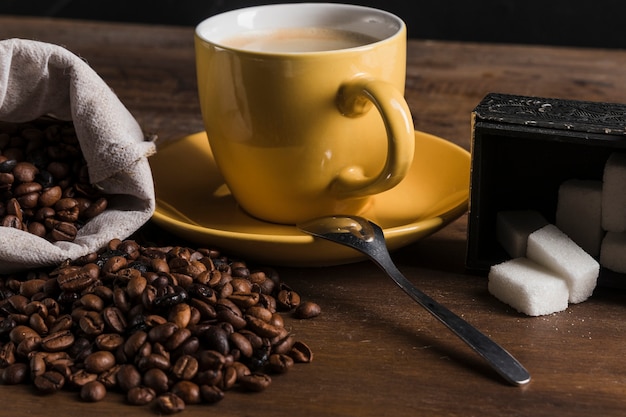 Foto gratuita taza cerca de azucarero y saco con granos de café.