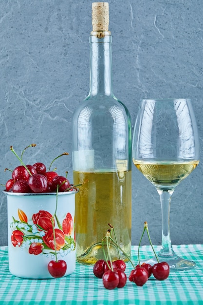 Foto gratuita taza de cerezas, botella de vino blanco y vidrio sobre superficie azul