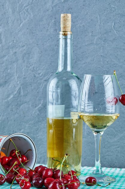 Taza de cerezas, botella de vino blanco y vidrio sobre superficie azul