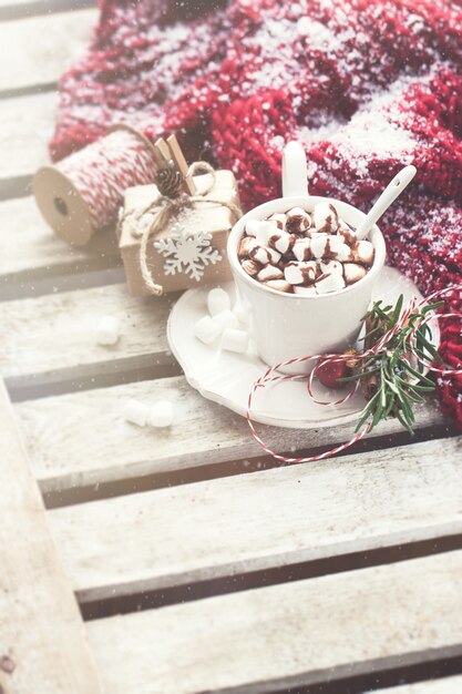 Taza con chocolate y malvaviscos con una bufanda con nieve