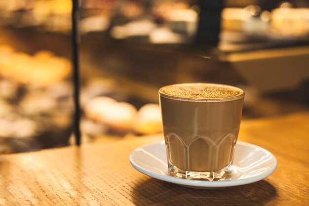 Taza de cristal deliciosa sabrosa del latte con el platillo en la tabla