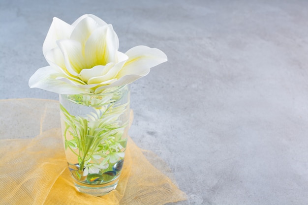 Una taza de cristal con una hermosa flor blanca sobre un mantel amarillo.