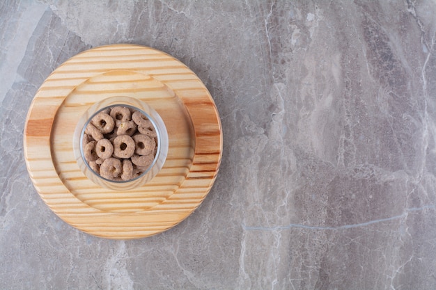 Una taza de cristal llena de anillos de cereal de chocolate sobre una tabla de madera.