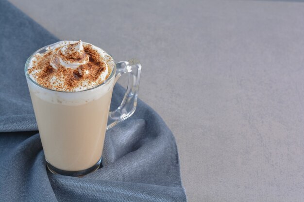 Una taza de delicioso café caliente decorado con cacao sobre tela azul.