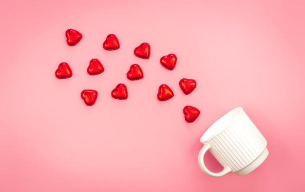 Foto gratuita una taza y dulces dispersos en forma de corazón sobre un fondo rosa yacía plano