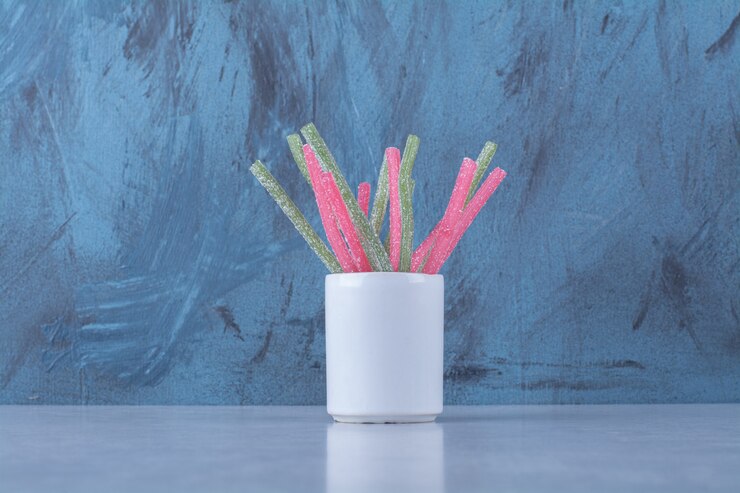Una taza con dulces de palitos de fruta de gelatina azucarada sobre fondo gris. Foto de alta calidad
