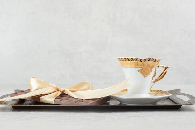 Taza de espresso con barra de chocolate atada con cinta en bandeja.