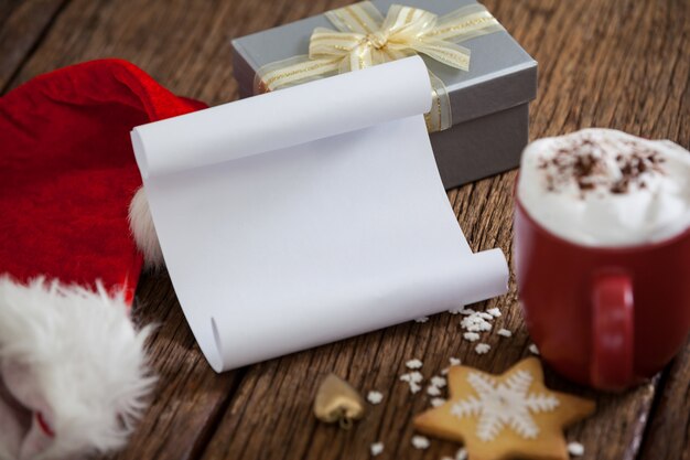 Taza con espuma, un sombrero de papa noel y un papel en blanco