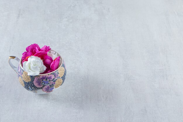 Una taza de flores púrpuras y blancas, sobre la mesa blanca.