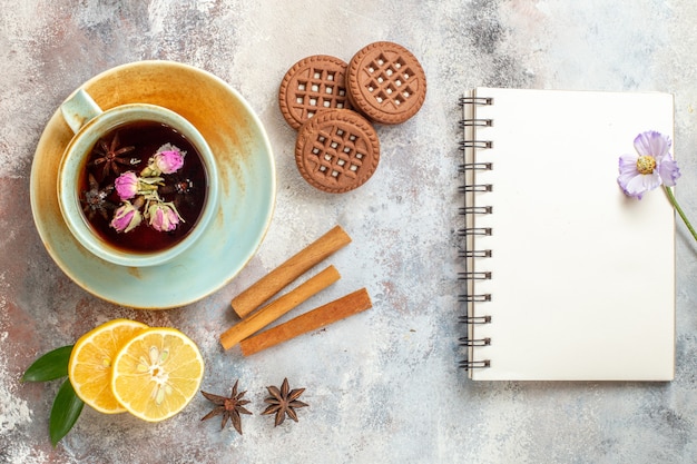 Una taza de galletas de té de hierbas y rodajas de limón limón canela y cuaderno en el cuadro blanco