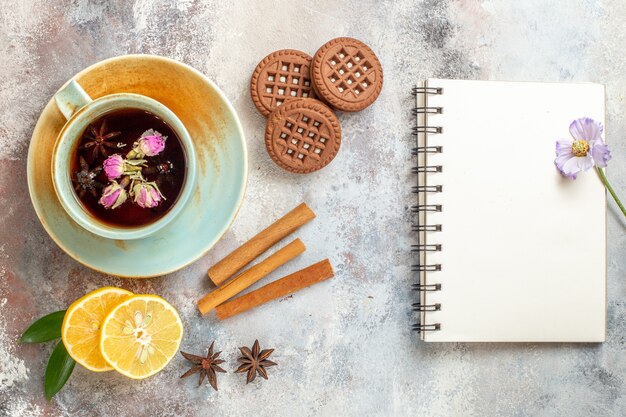 Una taza de galletas de té de hierbas y rodajas de limón limón canela y cuaderno en el cuadro blanco