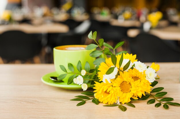 Taza hermosa de la flor y de café en el escritorio de madera con el fondo de la cafetería del defocus