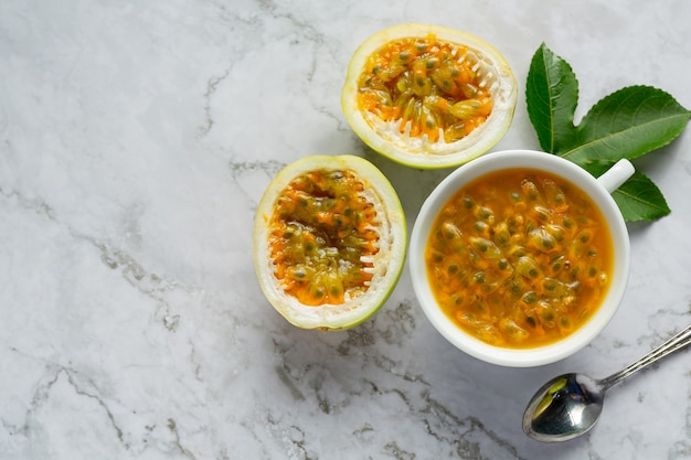 una taza de jugo de maracuyá y fruta de la pasión fresca cortada a la mitad en un piso de mármol blanco