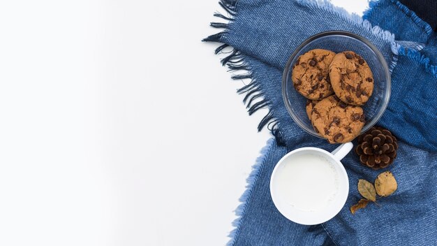 Foto gratuita taza de leche cerca de tazón de galletas en tela escocesa azul