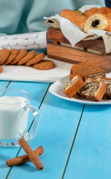 Una taza de leche con palitos de canela y una galleta en una mesa de madera azul.