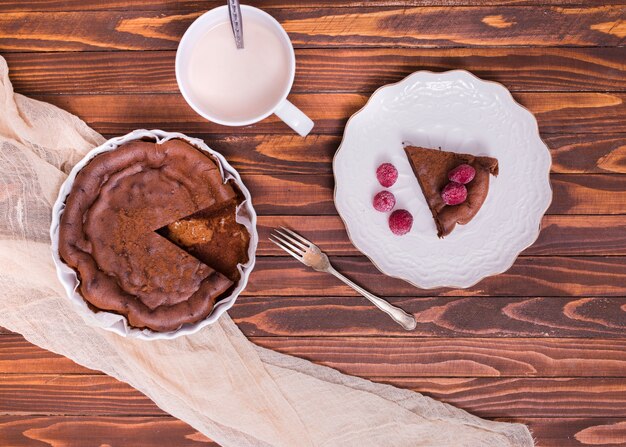 Taza de leche Rebanada de pastel y frambuesa en un plato de cerámica blanca sobre la superficie de madera