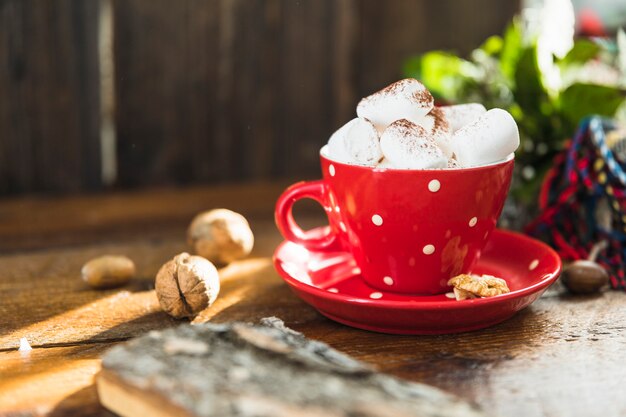 Taza con malvavisco en un plato cerca de las nueces