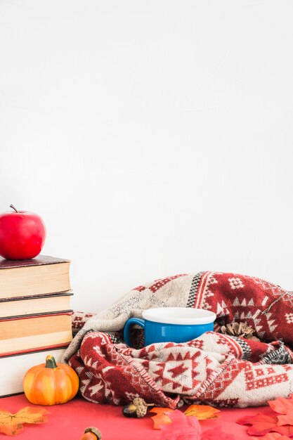 Taza y manta cerca de frutas y libros falsos