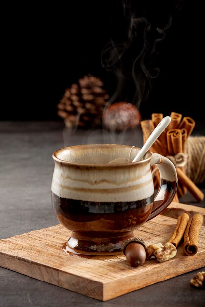 Taza marrón con palitos de canela y café sobre un soporte de madera