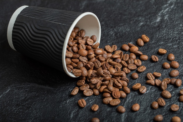 Una taza negra llena de granos de café sobre tabla de madera.