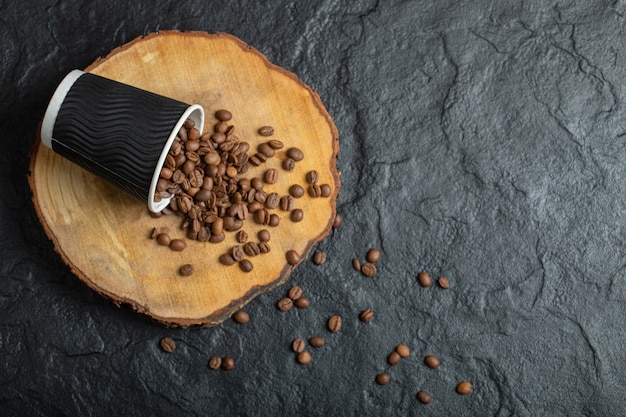 Una taza negra llena de granos de café sobre tabla de madera.