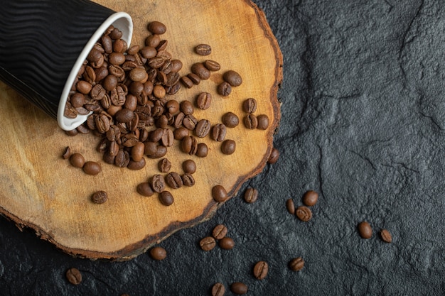 Una taza negra llena de granos de café sobre tabla de madera.