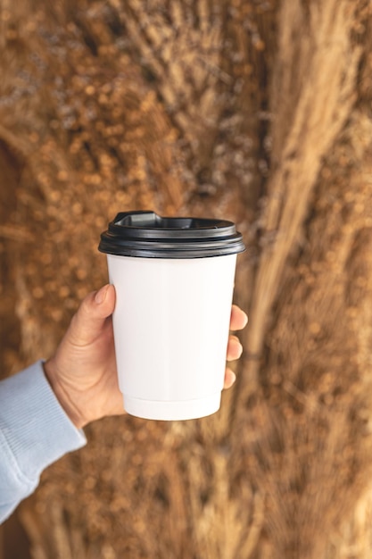 Taza de papel con café para ir sobre un fondo borroso de plantas de campo