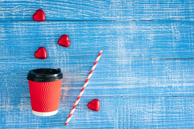 Foto gratuita taza de papel rojo y caramelos en forma de corazón sobre un fondo de madera azul