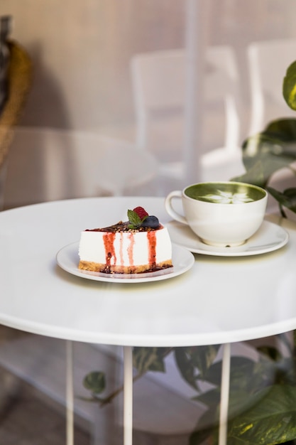 Taza y pastel de queso del latte del té verde de Matcha con la salsa de las bayas y la menta verde en la tabla blanca