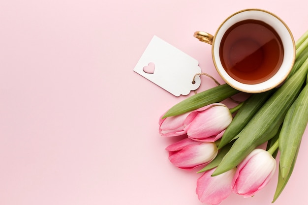 Taza plana con té junto a tulipanes