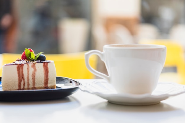 Taza y platillo de cerámica con una deliciosa rebanada de pastel en superficie blanca