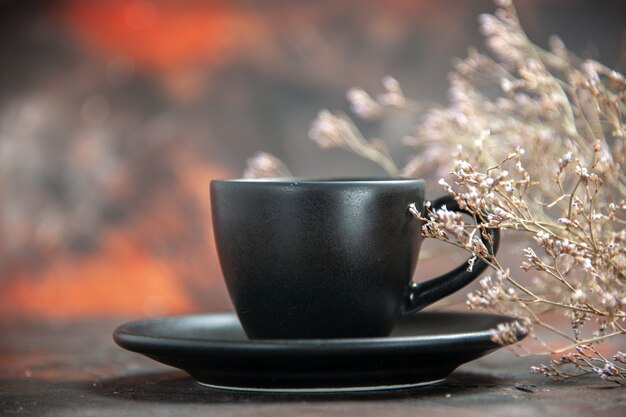 Taza y platillo negro de vista frontal en la mesa de color rojo oscuro con lugar libre