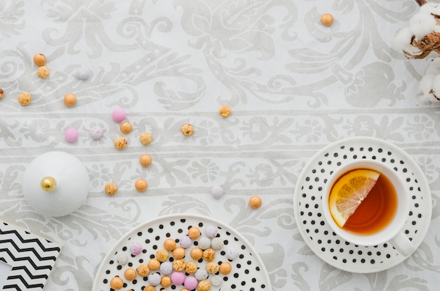 Taza y platillo de té de limón de jengibre con caramelos de colores sobre papel tapiz