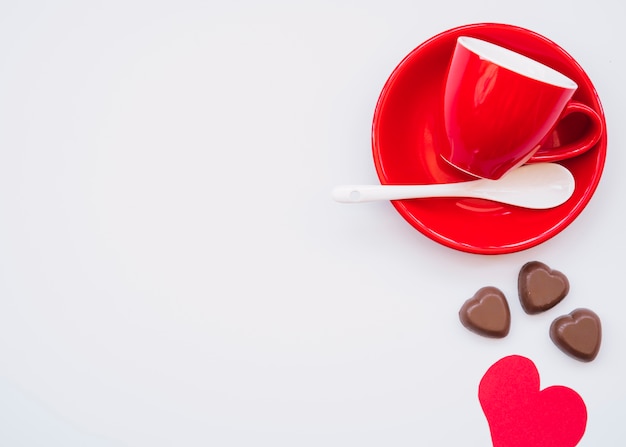 Taza en plato cerca de dulces de chocolate y tarjeta de San Valentín