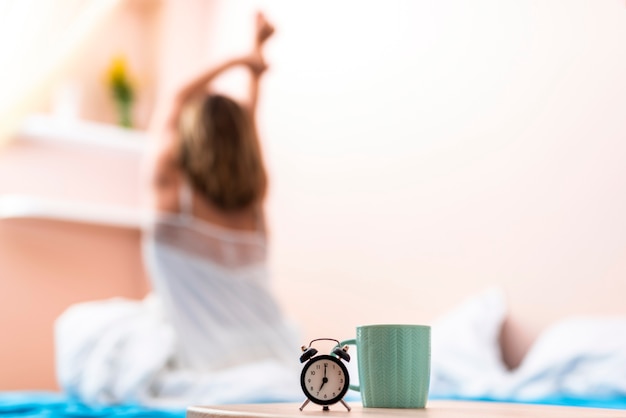 Taza de primer plano y reloj con una mujer que se extiende en el fondo